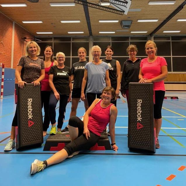 Gruppe von Frauen in Sportkleidung posiert auf einem blauen Gymnastikboden mit Reebok-Steppen.