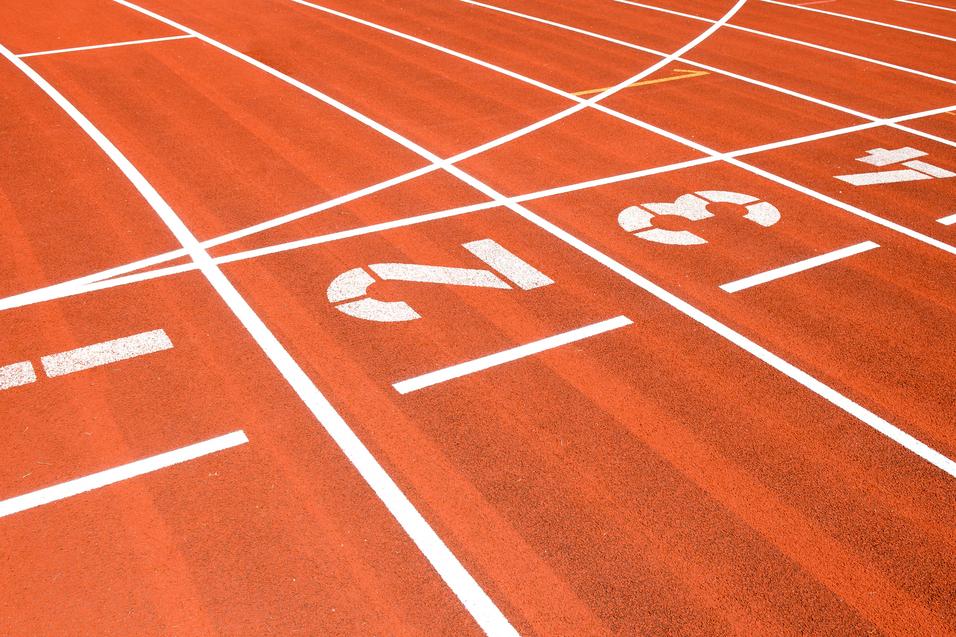 Nahaufnahme einer roten Laufbahn mit weißen Startnummern 1, 2, 3 und Markierungen für Laufstrecken.