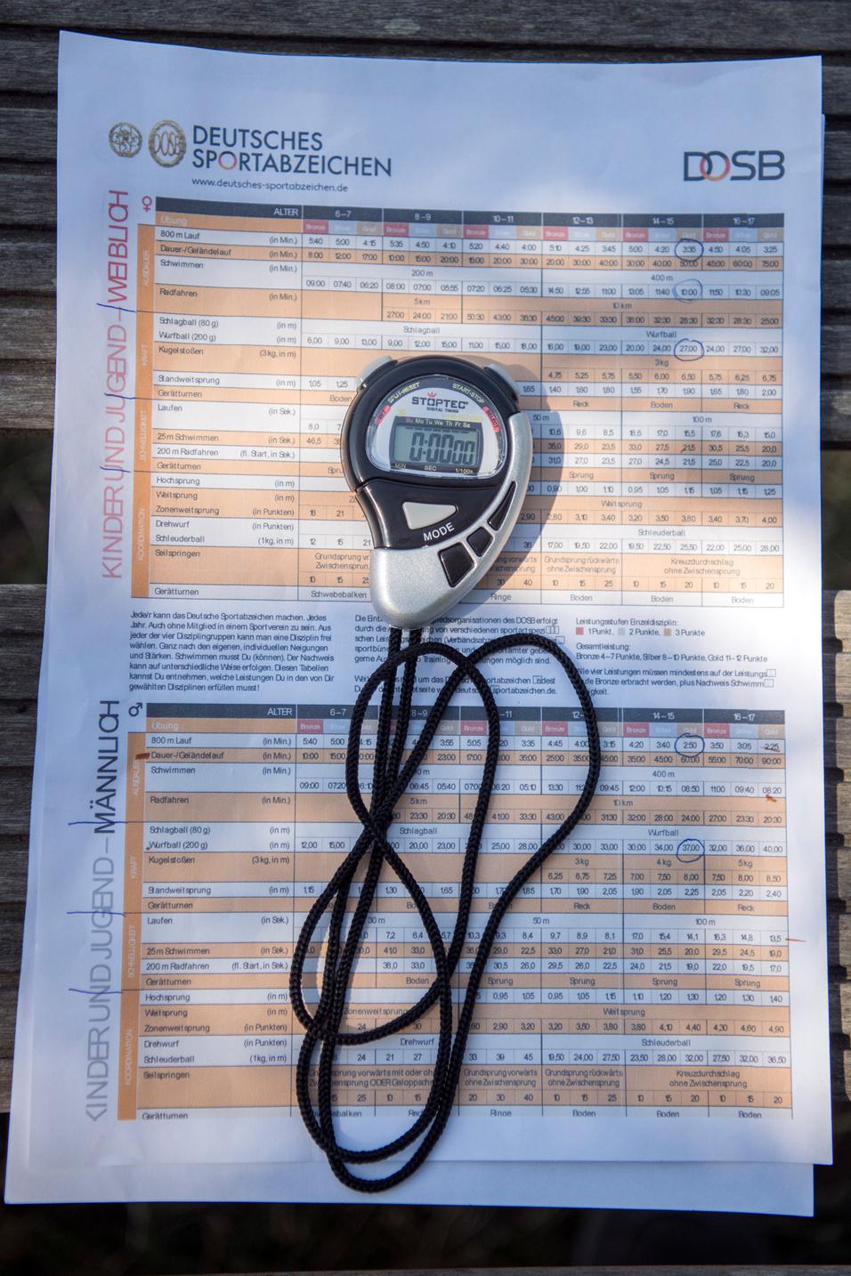 Stoppuhr und Infoblatt des Deutschen Sportabzeichens auf einer Holzbank im Freien.